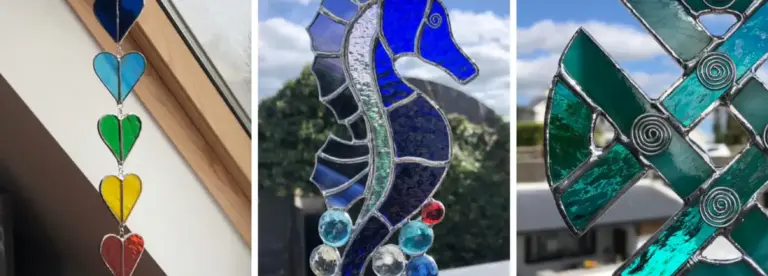 A collage of stained glass art: a hanging row of colourful heart shapes, a blue seahorse with glass bubbles, and a geometric green pattern, all displayed near windows with outdoor scenery visible.