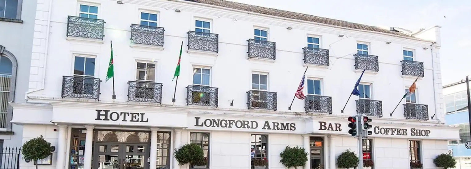 A three-storey white building with black iron balconies, several flags, and signs reading "Hotel," "Longford Arms," "Bar," and "Coffee Shop" above the entrances on the ground floor.