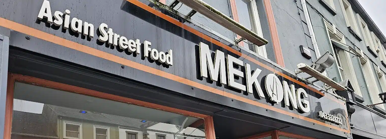 A restaurant sign reading "Asian Street Food MEKONG" is shown on the exterior of a building, with part of the street and other buildings reflected in the windows below.