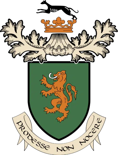 A green shield with a golden lion standing on hind legs, topped by an ornate crown and a black dog above it. Below the shield is a banner with the Latin motto "PRODESSE NON NOCERE.