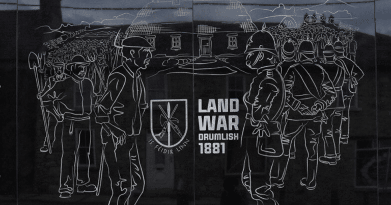 Line drawing on a plaque depicts men with tools facing armed officers in front of a building. Text reads “LAND WAR DRUMLISH 1881” with an emblem and Irish phrase, referencing an historical event.