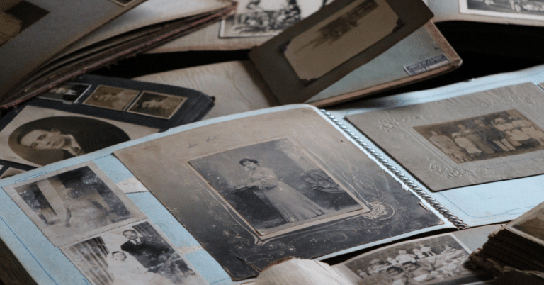 Several vintage photo albums are open, displaying black-and-white and sepia photographs of people, including portraits and group photos, on a wooden surface.